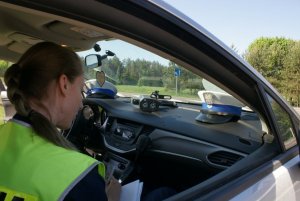 radiowóz z otwartym oknem przez, które widać czapkę funkcjonariusza ruchu drogowego i tarczę policyjną
policjant mierzy prędkość fotoradarem
policjantka siedzi i  pisze w radiowozie